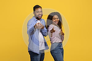 Happy Couple Pointing Towards Camera Against a Bright Yellow Background