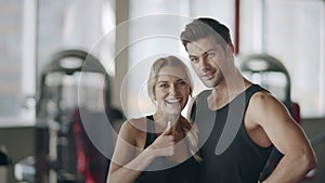 Happy couple posing in modern gym. Smiling woman showing thumbs up gesture.