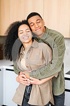 Happy couple posing over blurred kitchen background. Happy owners of new flat smiling with closed eyes. Young handsome