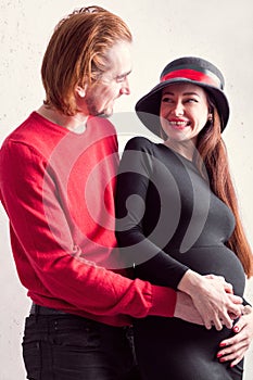 Happy couple of pregnant girl who stands with her husband and hold together herself tummy