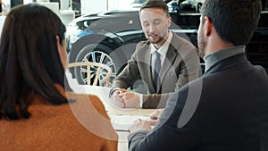 Happy couple purchasing car signing contract doing high-five talking to sales manager