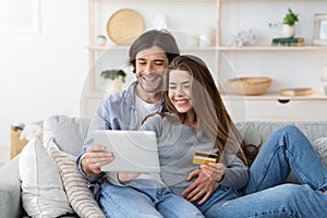 Happy couple purchasing online, holding credit card and digital tablet