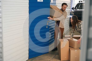 Young man and woman with big cardboard boxes in self storage unit