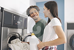 Happy couple putting laundry into washing machine at public laundromat