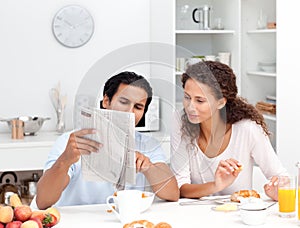 Happy couple reading the newspaper at breakfast