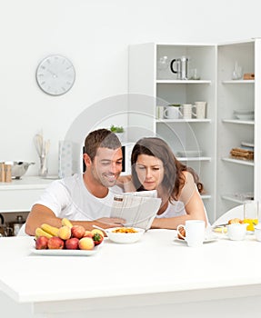 Happy couple reading the newspaper in the kitchen