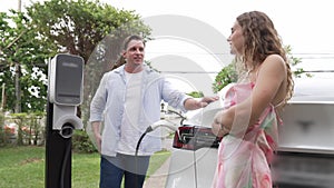 Happy couple recharge electric vehicle from EV charging station. Fastidious