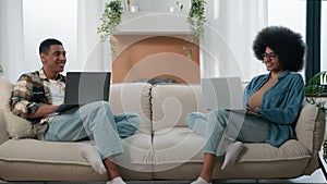 Happy couple relax at couch at home with laptop internet overuse freelancers African American man with woman smiling