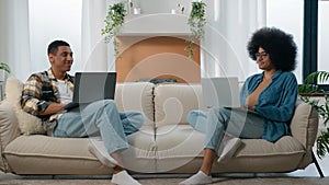 Happy couple relax at couch at home with laptop internet overuse freelancers African American man with woman smiling