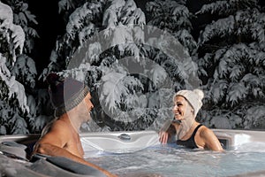 Happy couple relaxing in outdoor hot tub at winter with snowy trees in background. spa resort