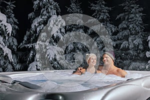 Happy couple relaxing in outdoor jacuzzi at winter in resort spa hotel. romantic getaway