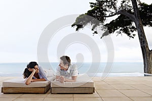 Happy Couple Relaxing On Sunbeds By Infinity Pool