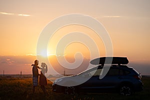 Happy couple relaxing beside their SUV car during honeymoon road trip at sunset. Young man and woman enjoying time together