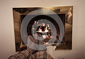 Happy couple relaxing under blanket by the fireplace warming up feet in woolen socks