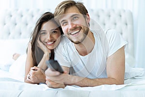 Happy couple with remote lying in bed at home and watching tv.