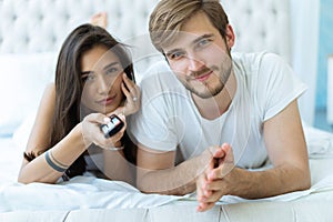 Happy couple with remote lying in bed at home and watching tv.