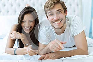 Happy couple with remote lying in bed at home and watching tv.