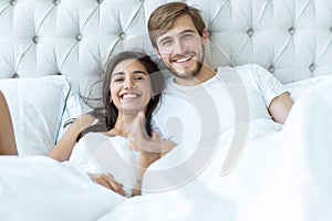 Happy couple with remote lying in bed at home and watching tv.