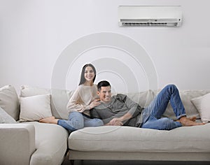 Happy couple resting under air conditioner on white wall at home