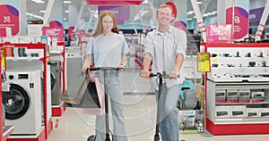 Happy Couple Riding Scooter at Home Electronics Store.