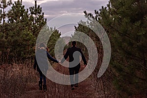 Happy couple running through forest holding hands. Man in coat and a young woman are fooling around