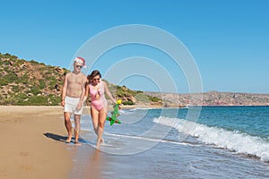 Happy couple in Santa hat walking on the beach with inflatable Christmas tree. Christmas vacation concept