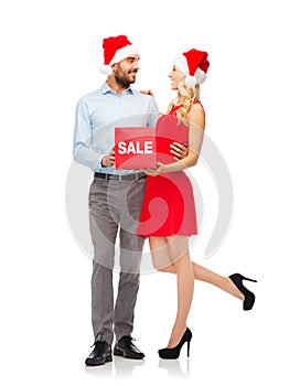 Happy couple in santa hats with red sale sign