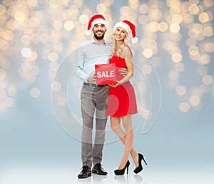 Happy couple in santa hats with red sale sign