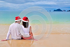 Happy couple in Santa hats relaxing on tropical sandy beach near sea, Christmas and New Year holiday vacation