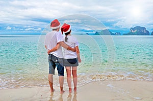 Happy couple in Santa hats relaxing on tropical sandy beach near sea, Christmas and New Year holiday vacation