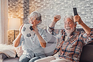 Happy couple of seniors or football fans watching soccer on tv and celebrating victory at home. Family, sports and entertainment