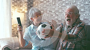 Happy couple of seniors or football fans watching soccer on tv and celebrating victory at home. Family, sports and entertainment