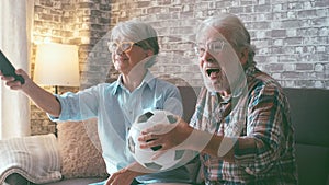 Happy couple of seniors or football fans watching soccer on tv and celebrating victory at home. Family, sports and entertainment