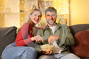 Happy couple sharing popcorn on cozy sofa