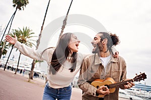 Happy couple singing and dancing playing the ukulele outdoors at the city.