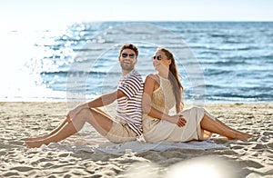 happy couple sitting back to back on summer beach