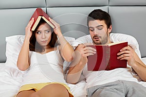 Happy Couple Sitting in Bed Reading Books at Home in Bedroom