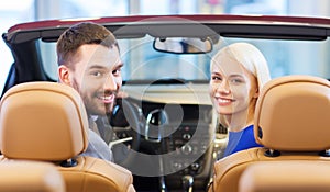 Happy couple sitting in car at auto show or salon