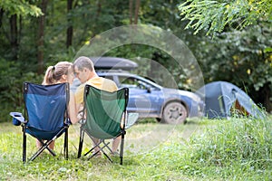 Happy couple sitting on chairs at campsite hugging each other. Travel, camping and vacations concept