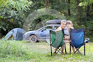 Happy couple sitting on chairs at campsite relaxing together. Travel, camping and vacations concept