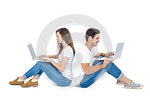 Happy couple sitting on the floor back to back using laptop