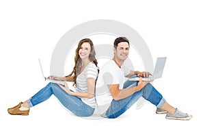 Happy couple sitting on the floor back to back using laptop