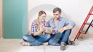 Happy young couple sitting on floor at house under construction and using digital tablet