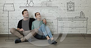Happy couple sitting on floor in new house and planning new home interior. furniture sketch