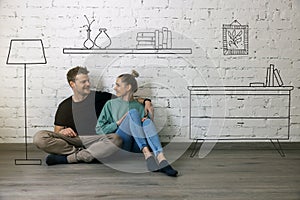 Happy couple sitting on floor and planning new home interior. furniture sketch