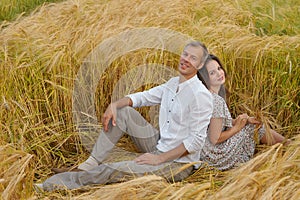 Happy couple sitting on the grass in a wheat field