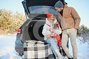 Happy couple sitting in open car back, having stop off. Romantic traveling concept. Winter forest