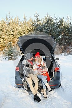 Happy couple sitting in open car back, having stop off. Romantic traveling concept. Winter forest