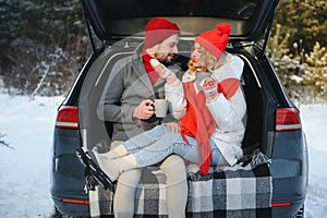 Happy couple sitting in open car back, having stop off. Romantic traveling concept. Winter forest