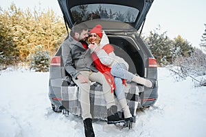 Happy couple sitting in open car back, having stop off. Romantic traveling concept. Winter forest